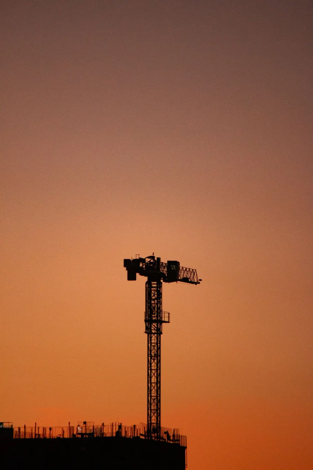 A tower crane against an orange dusk sky
